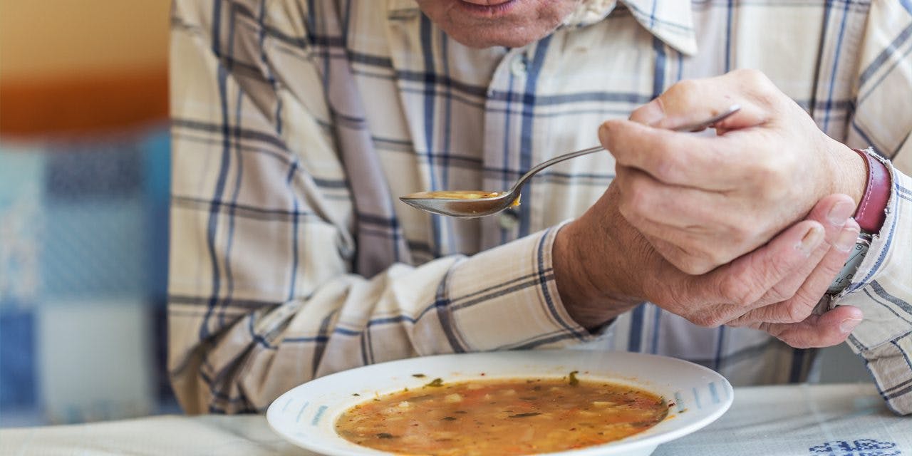 old man holding his other hand while eating