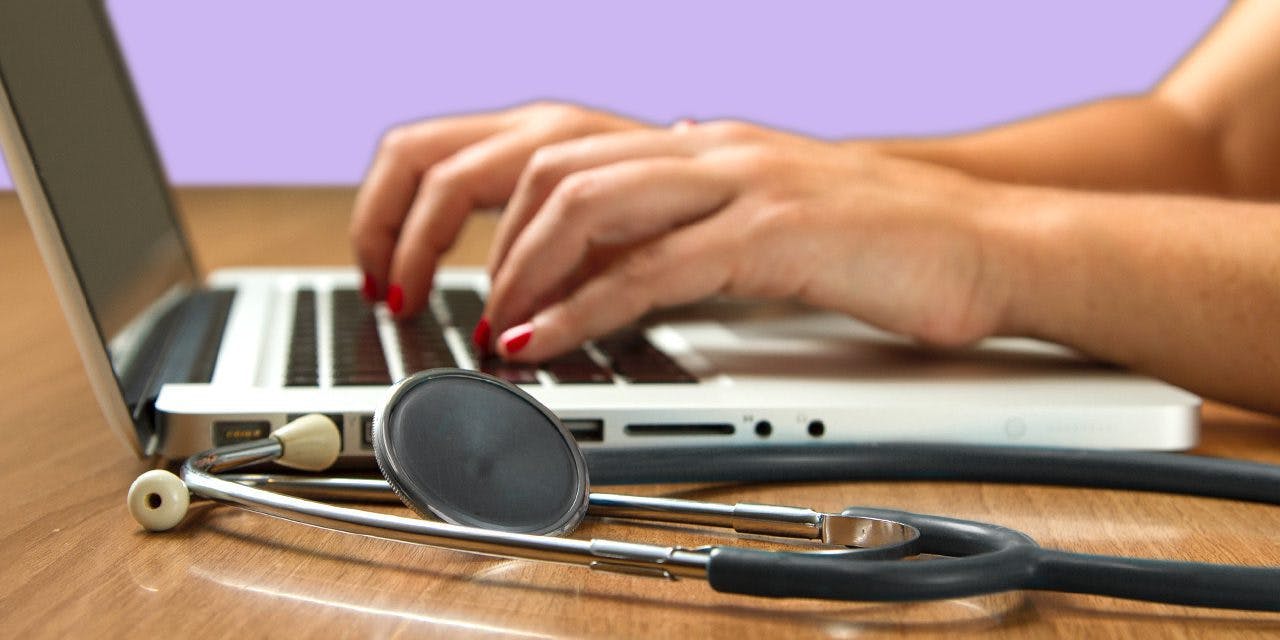 closeup woman's hands typing on her laptop beside a stethoscope
