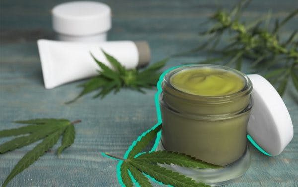 crema de color verde en un tarro rodeado de hojas de cannabis