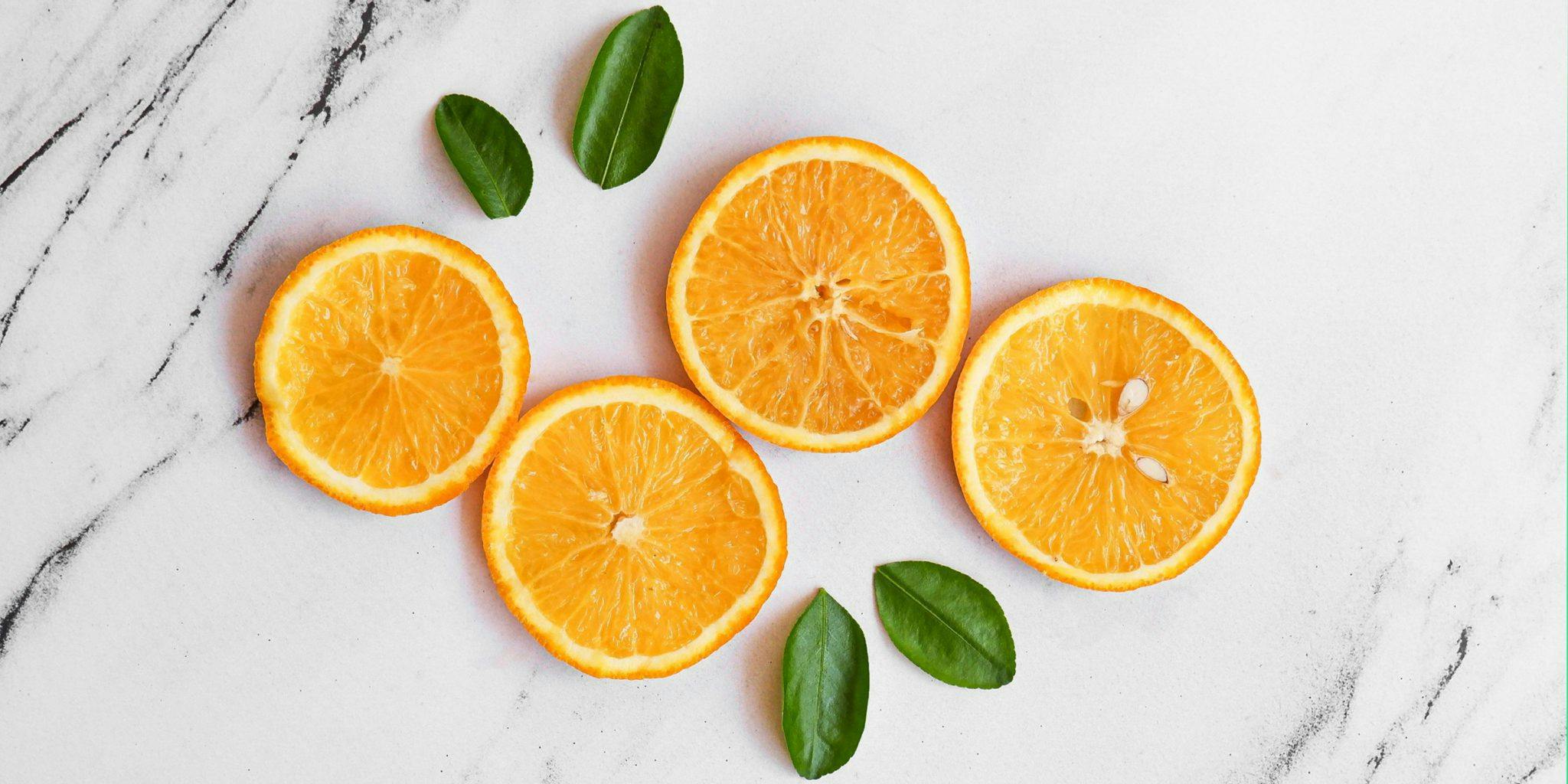 four slices of orange with scattered leaves in a white bg