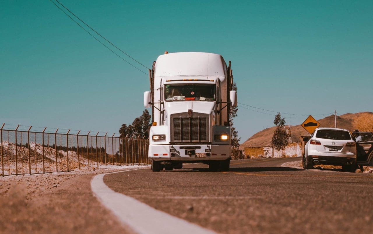 big white truck crossing the street with white car stopped on the other side