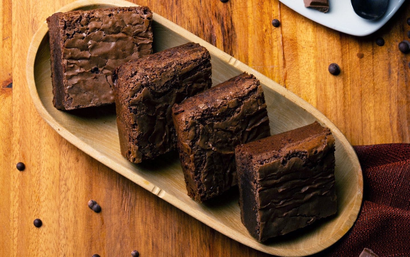 four brownies arranged inside a wooden oblong plate in wooden table