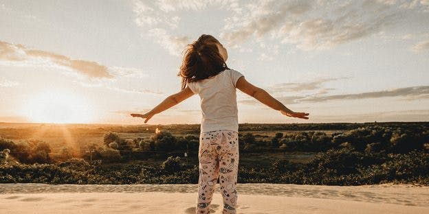 a child facing sunset while spreading her arms