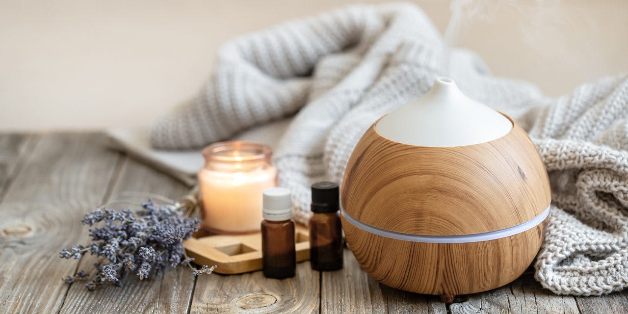 diffuser surrounded by blanket, lavender branch, candle and essential oils