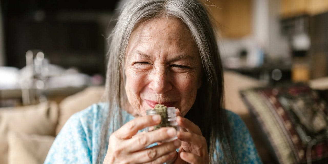 old woman holding and smelling weed in a small clear container