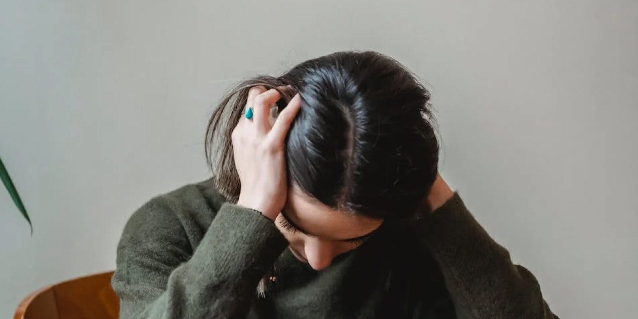 a woman with hands in her hair looking in pain or frustrated