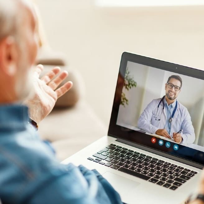 From above elderly male making video call to medical practitioner and speaking while sitting on couch at home